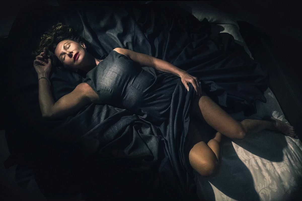 Claudia Hackman resting on a bed in a dimly lit room.