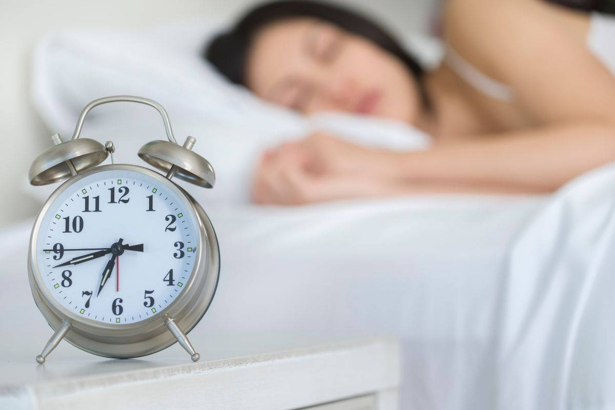 A woman peacefully sleeping in bed with an alarm clock nearby, ready to wake her up